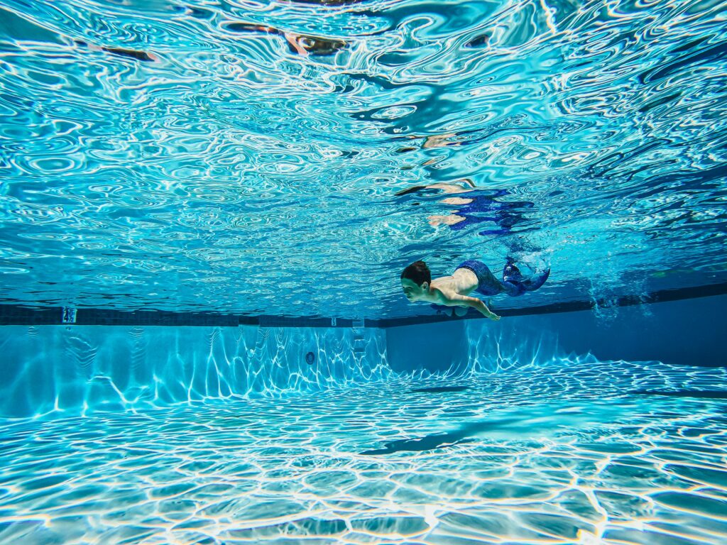 Captivating underwater photo of a child swimming with a mermaid tail in a bright pool.