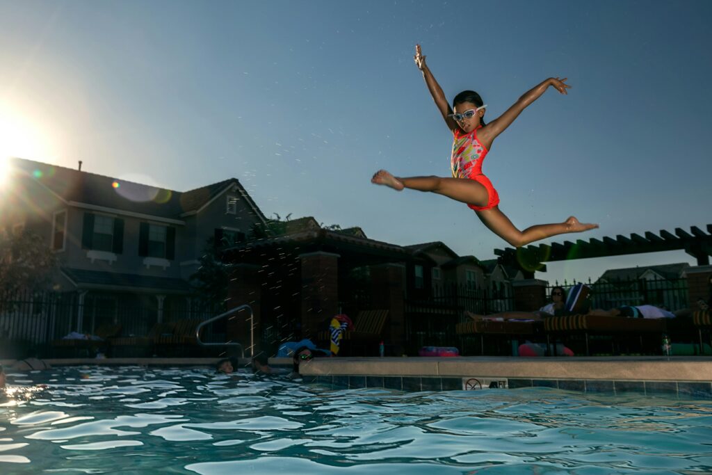 A young girl in a swimsuit jumps into a swimming pool at sunset, capturing summer fun.