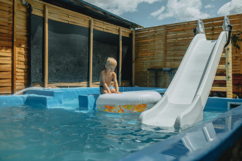 Young child playing with inflatable in a pool with slide during summer.