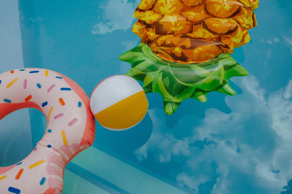Vibrant inflatable donut, pineapple, and beach ball float in a summer pool.
