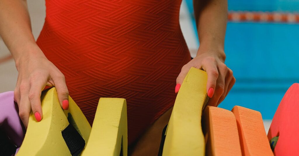 A woman in a red swimsuit arranging colorful swim kickboards by a swimming pool.